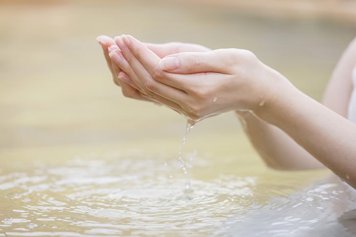 温泉の湯を救う女性の手