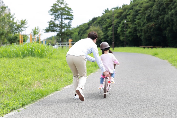 自転車の練習をする親子（出典：pixta.jp）