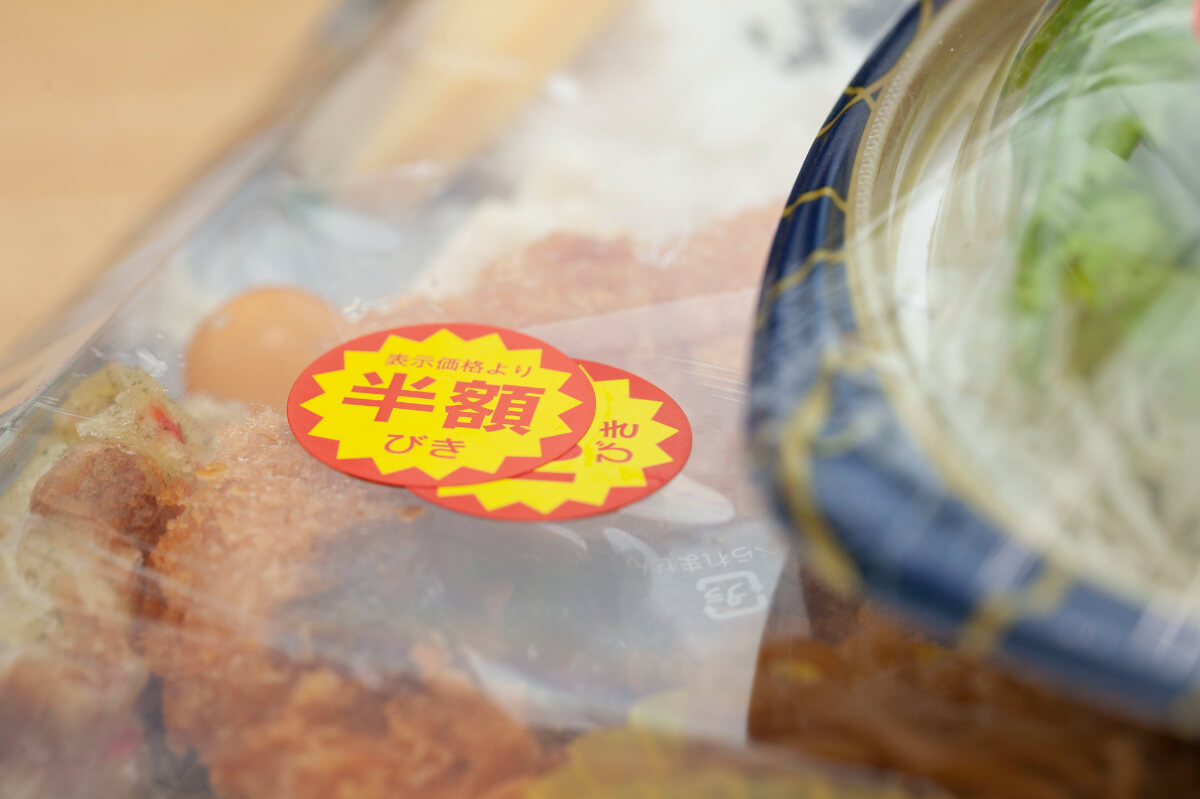 半額シールが貼られたスーパーのお弁当と総菜（出典：pixta.jp）