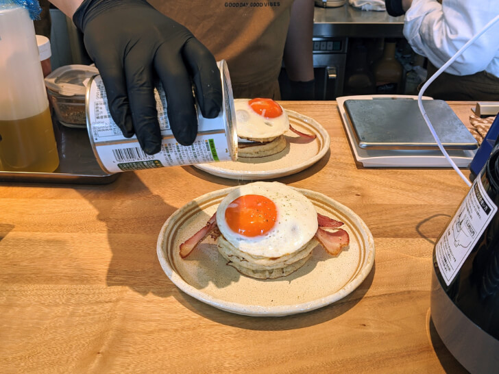 ベーコンエッグパンケーキにスパイスを振る様子