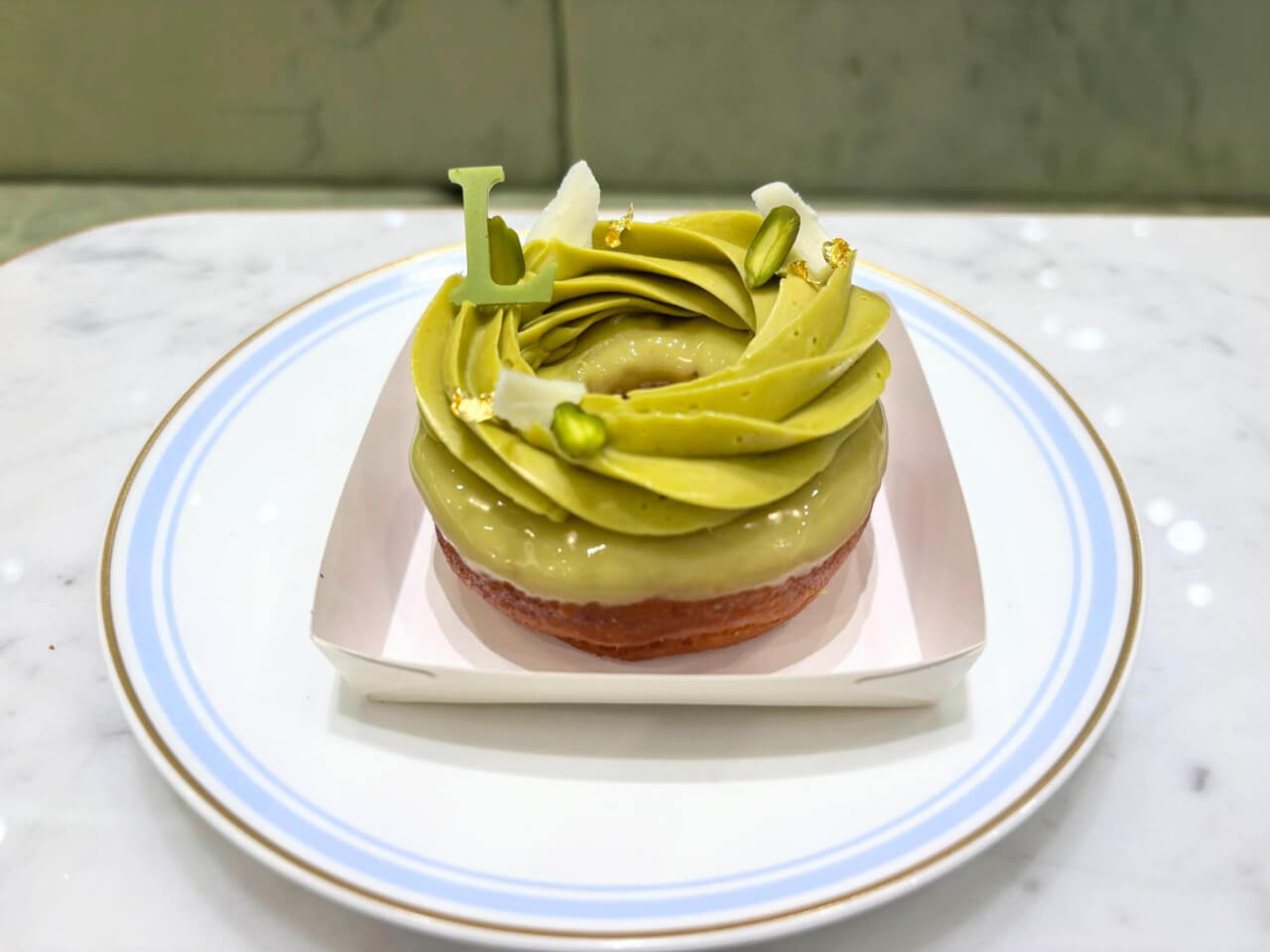 バタークリーム、金箔、Lのチョコレートが飾られたピスタッシュのドーナツ